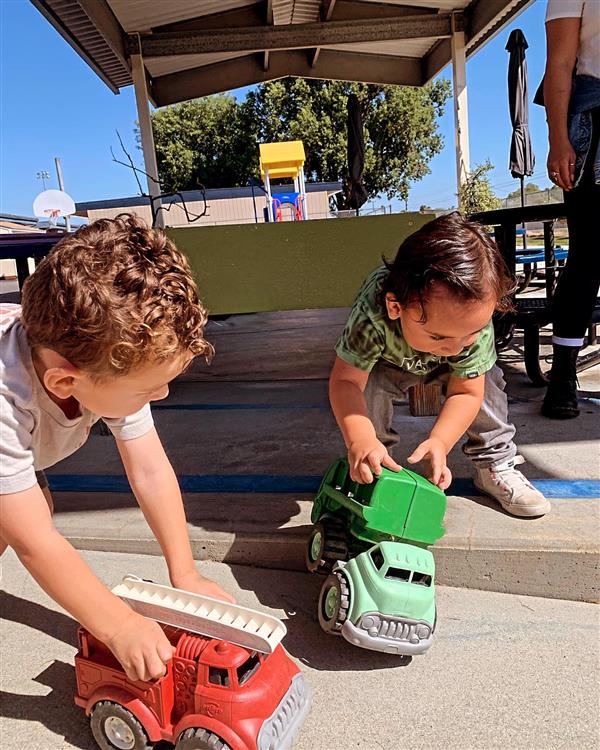 Two students playing with trucks on the playground.